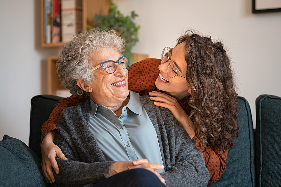 An older woman in a senior living community in Texas smiles at a younger woman while they hug.